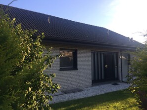 Une maison avec un toit en tuiles, une façade en briques, une porte d’entrée et une fenêtre.