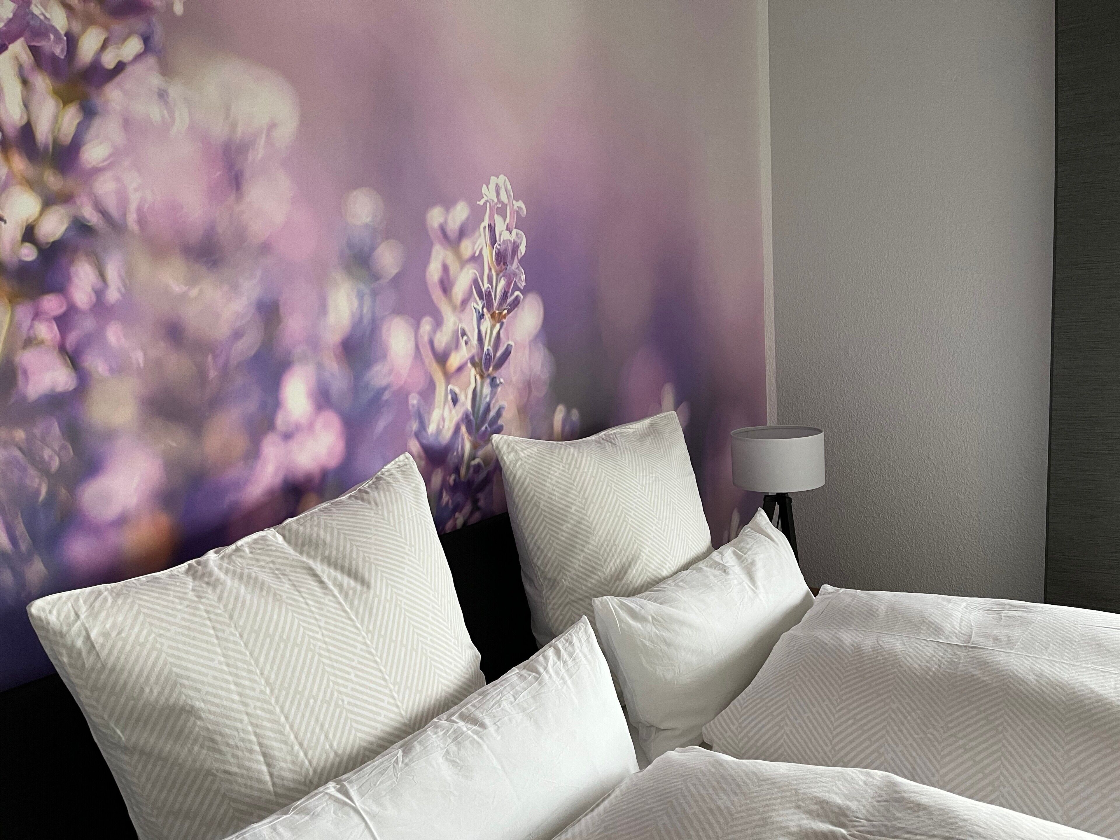 A hotel room with a bed, pillows, a lamp, and a wall with a floral mural.