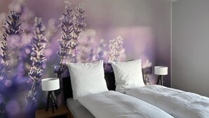 A bedroom with a bed, two bedside tables, and a wall mural. - Haus Blumenglück "Lavender and Dandelion" – Two Apartments for up to 11 Guests (Herscheid)