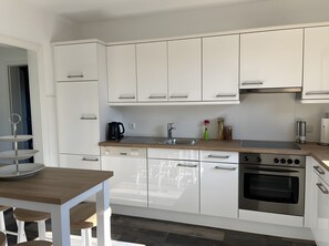 Eine moderne Küche mit weißen Schränken, einer Holz Arbeitsplatte, einer Spüle, einem Wasserkocher und einem Backofen.