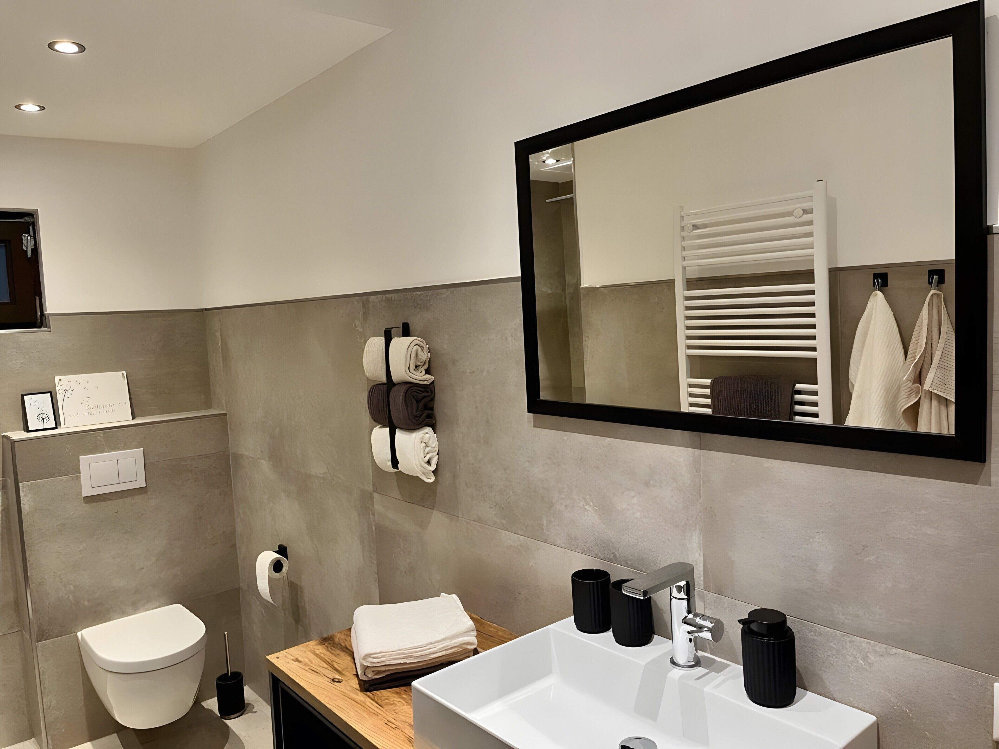 Ein modernes Badezimmer mit einem weißen Waschbecken, einem Spiegel, einem Handtuchhalter und einer Toilette.