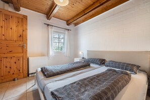 Un dormitori amb dos llits, bigues de fusta, una paret de maó blanc i una finestra amb cortines.