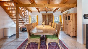A dining area with a wooden table, wicker chairs, a red patterned rug, and a staircase. - Holiday Home 'Mittelhuus' with Private Terrace, Private Garden and Wi-Fi (Wangerland)