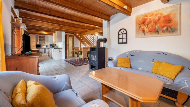 A cozy living room with a sofa, chairs, a wooden table, a fireplace, and a kitchen in the background. - Holiday Home 'Mittelhuus' with Private Terrace, Private Garden and Wi-Fi (Wangerland)