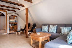 Ein gemütliches Loft-Zimmer mit einer Holzbücherwand, einem Sofa, einem Sessel und einem kleinen Tisch.