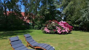 Dos sillones de descanso en un área con césped, un parterre floral y árboles al fondo.