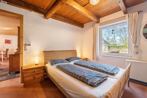 Ein Schlafzimmer mit zwei Betten, einem Holzkopfstück, Nachttischen mit Lampen, einem Fenster mit Vorhängen und einer herzförmigen Dekoration an der Wand.