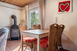 Ein gemütliches Zimmer mit Tisch, Korbstühlen, Kamin und einem fenster mit Vorhängen.