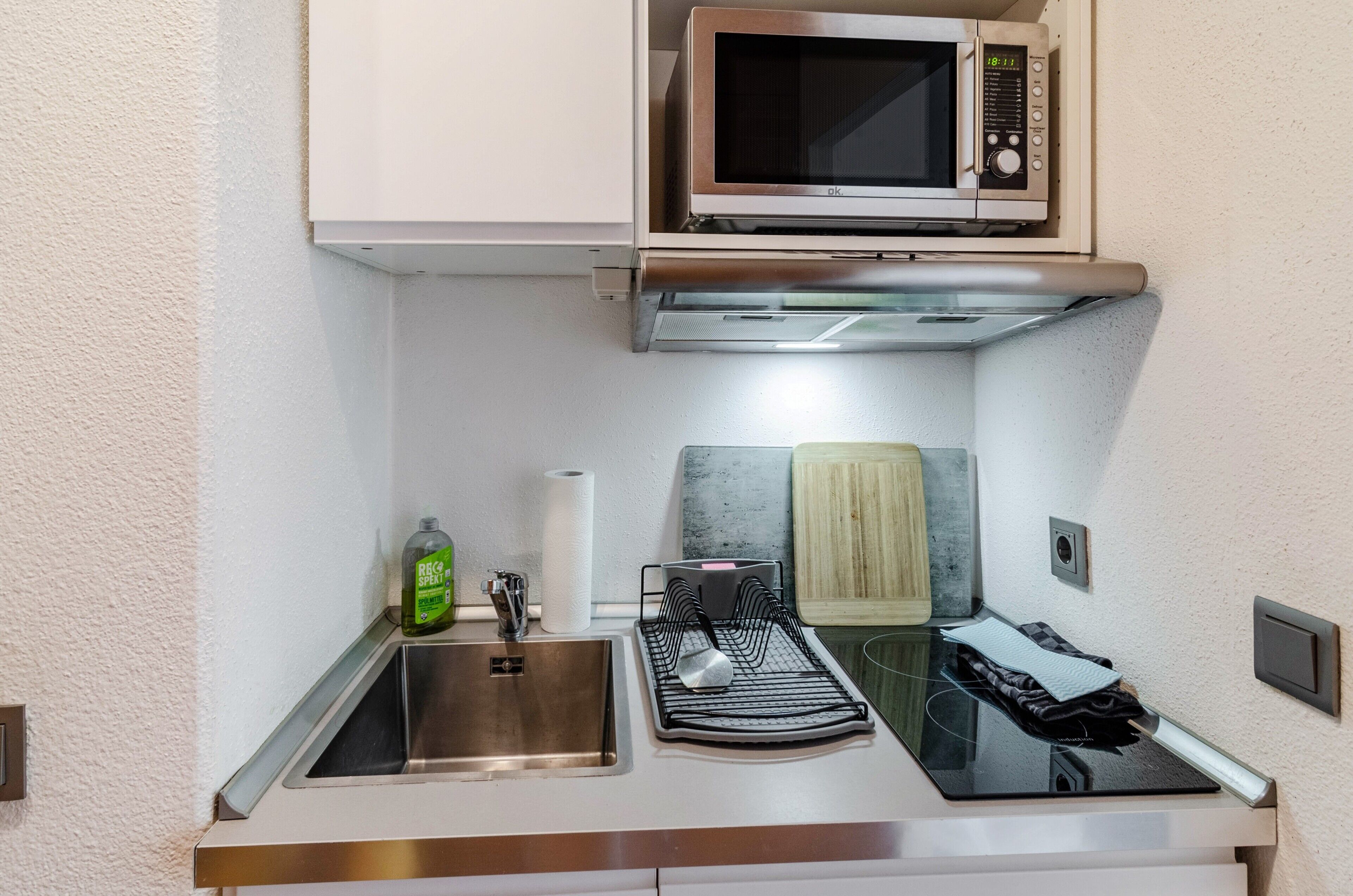 Una kitchenette compacta con microondas, fregadero, escurreplatos y toallero.