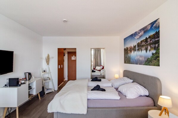 A hotel room with a bed, a desk with a computer, a TV, and a painting of a landscape.
