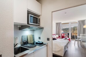 A compact hotel room with a kitchenette, a bed, a dining area, and a view of the outdoors. - Apartment 'Eure Auszeit' with Lake View, Shared Garden and Wi-Fi (Goslar)