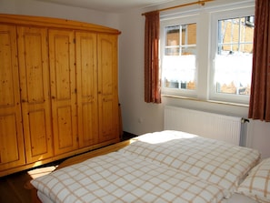 Une chambre à coucher avec un lit, une armoire en bois, une fenêtre avec des rideaux et un radiateur.