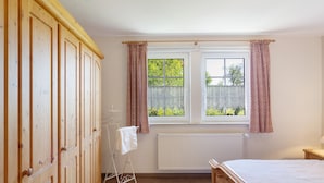 A bedroom with a wooden wardrobe, a radiator, a window with curtains, and a bed. - Apartment 'Die Fuchsmühle' with Shared Terrace, Shared Garden and Wi-Fi (Liebenau)