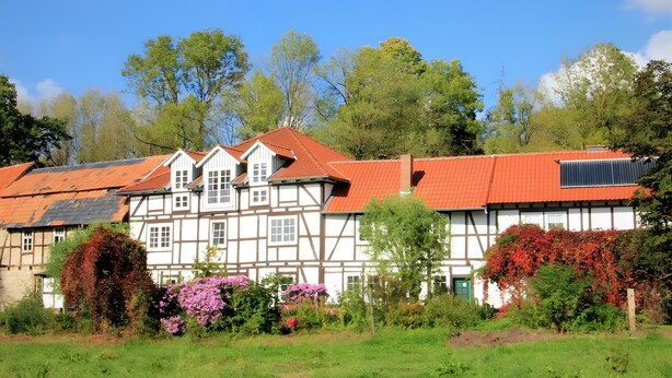 A traditional half-timbered building with a red roof, surrounded by lush greenery and flowering plants. - Apartment 'Die Fuchsmühle' with Shared Terrace, Shared Garden and Wi-Fi (Liebenau)