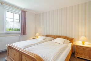 A double bed with a wooden headboard, two bedside tables with lamps, a window with a curtain, and striped wallpaper.