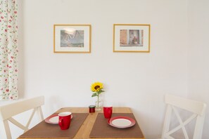 Uma mesa de jantar com duas cadeiras, um vaso com um girassol e duas fotos emolduradas na parede.