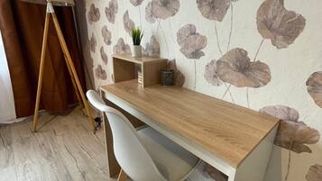 A wooden desk with a white chair, a small plant, and a lamp in a room with floral wallpaper and wooden flooring.