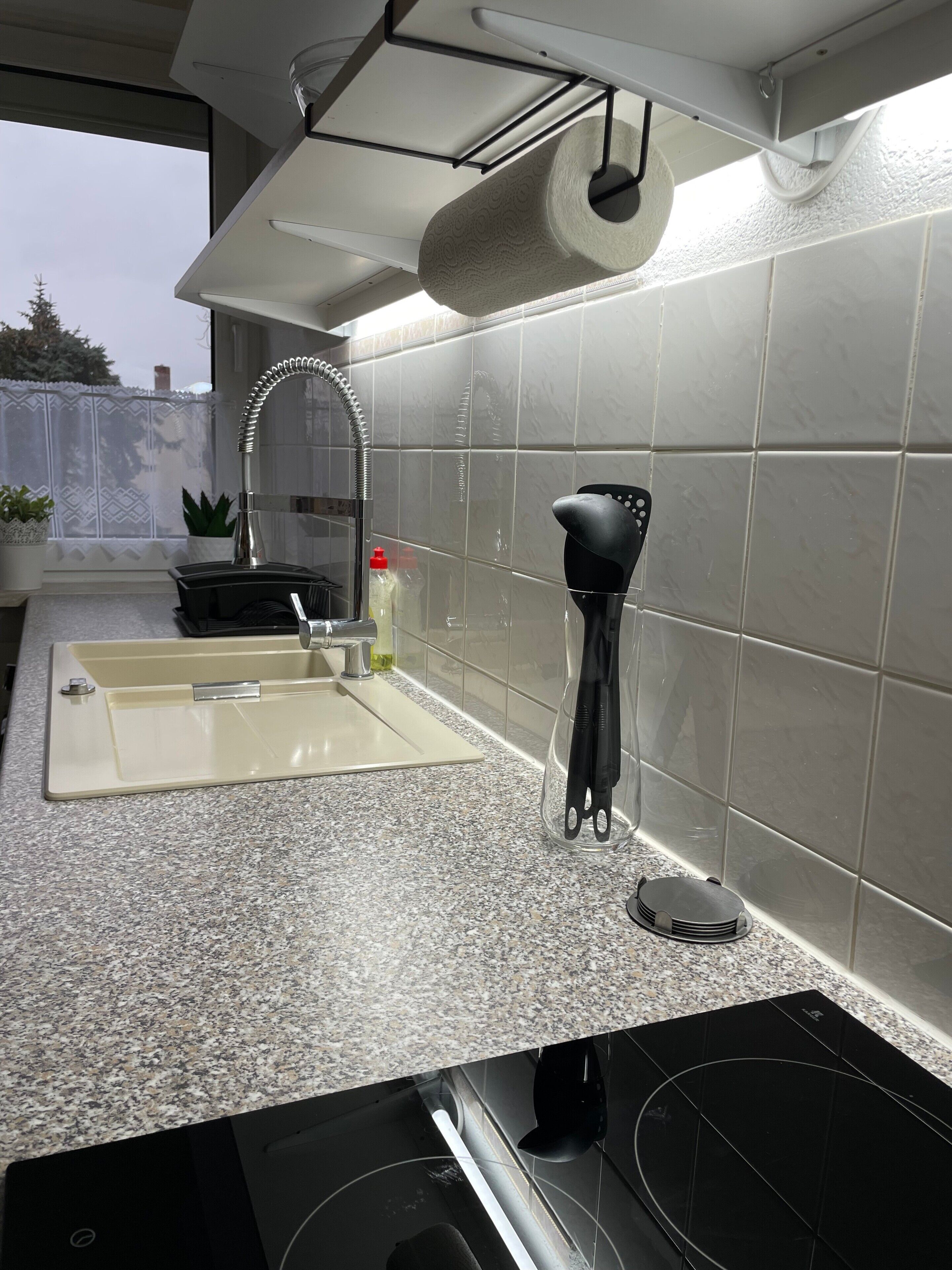 A kitchen with a granite countertop, a stainless steel sink, a black range hood, and a window with a view of trees.