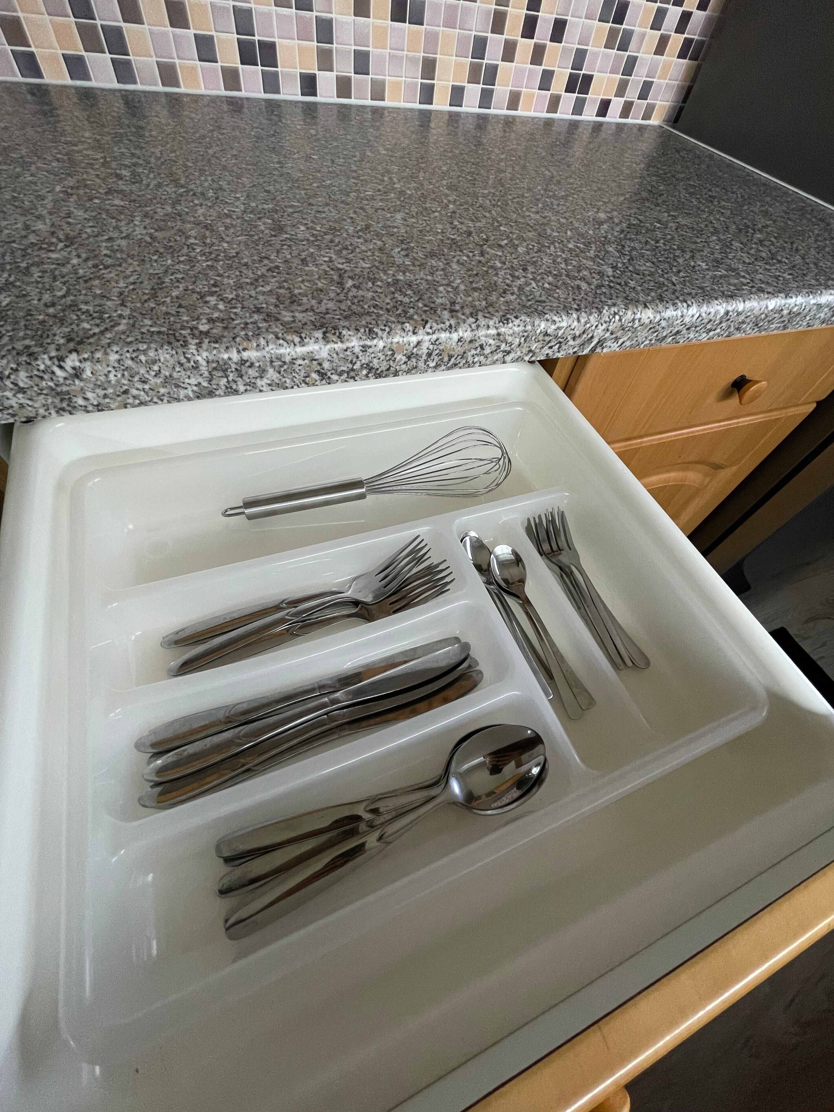 A kitchen with a granite countertop, a white sink with utensils, and a wooden cabinet.