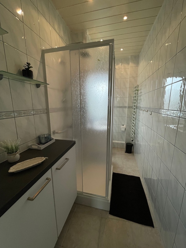 A modern kitchen with white cabinets, a black countertop, and a glass shower enclosure.