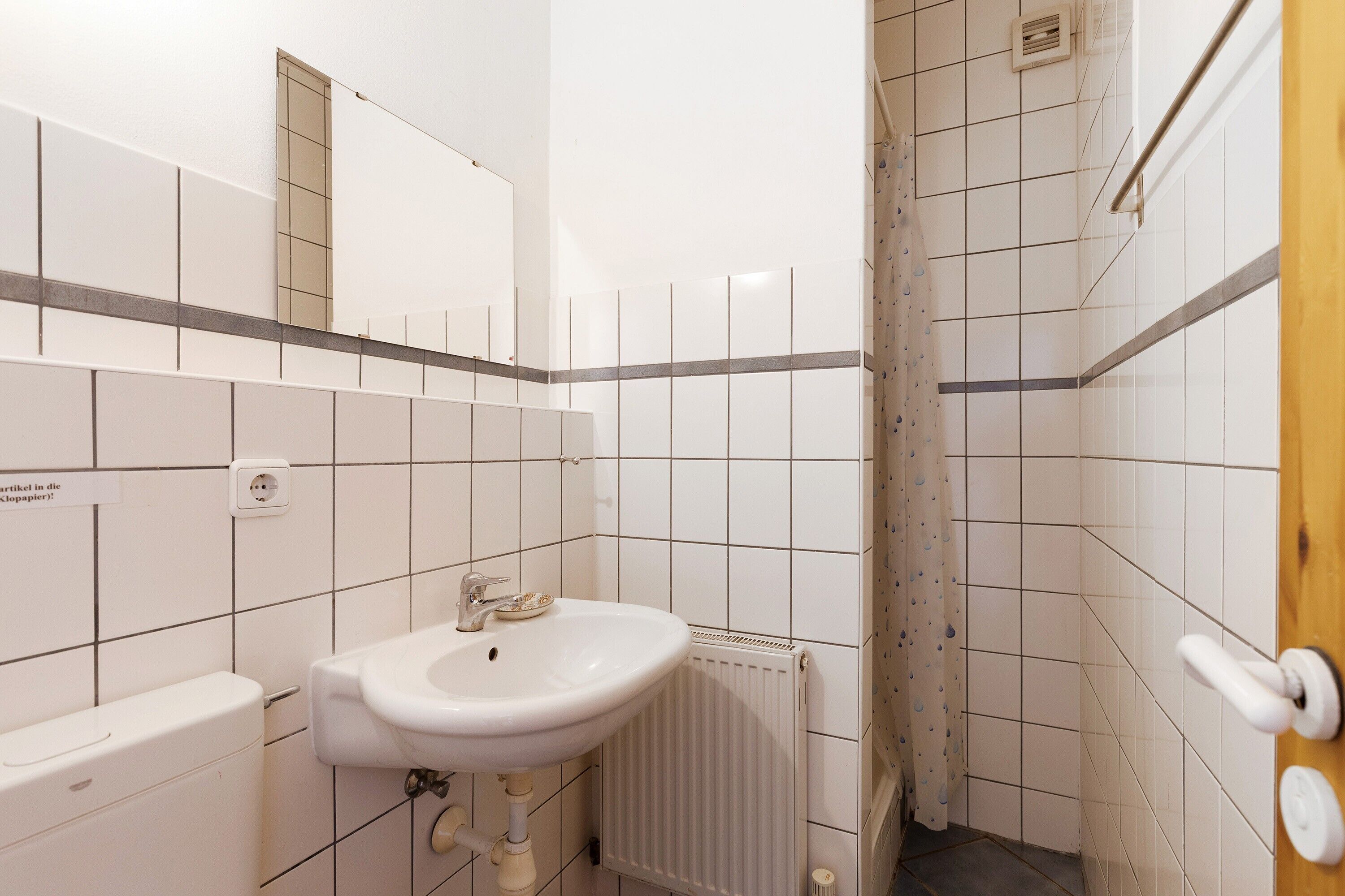 Une salle de bain avec un lavabo blanc, un miroir, des toilettes et un espace douche.