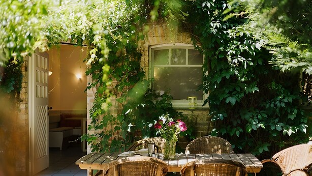 A rustic outdoor seating area with wicker furniture, a stone wall, and a window overlooking a garden. - Finca 'Gottsdorf' with Private Terrace and Shared Garden (Nuthe-Urstromtal)