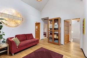 Una habitación amplia con un sofá rojo, un mueble de madera y una lámpara fijada a la pared.