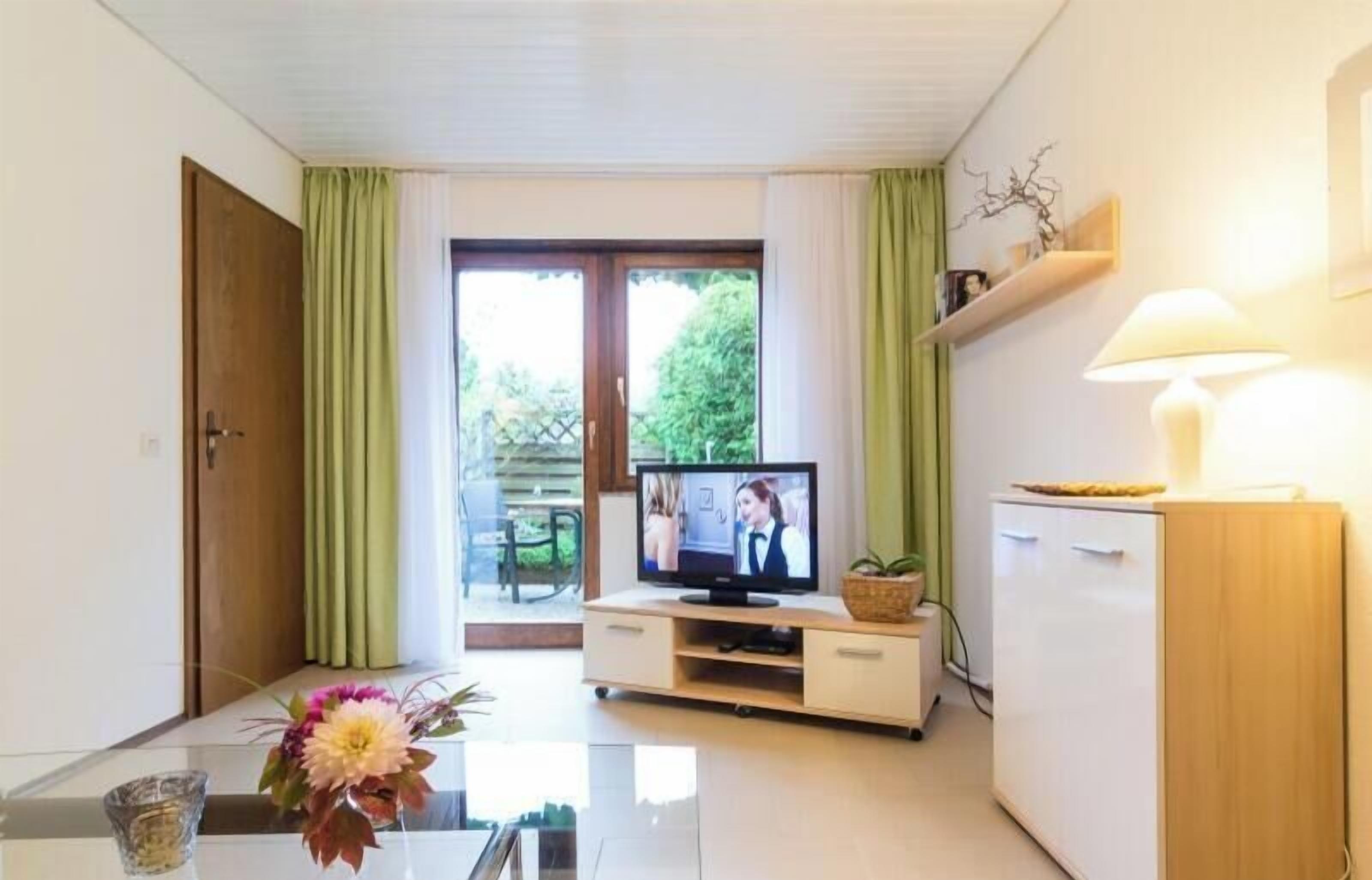 Ein Zimmer mit Fernseher, einem Esstisch mit Blumen, einem Schrank und einer Glastür zum Außenbereich.