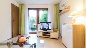 A room with a television, a dining table with flowers, a cabinet, and a sliding glass door leading to an outdoor area. - Apartment 'Bergfrieden' with Private Terrace, Shared Garden and Wi-Fi (Bad Herrenalb)
