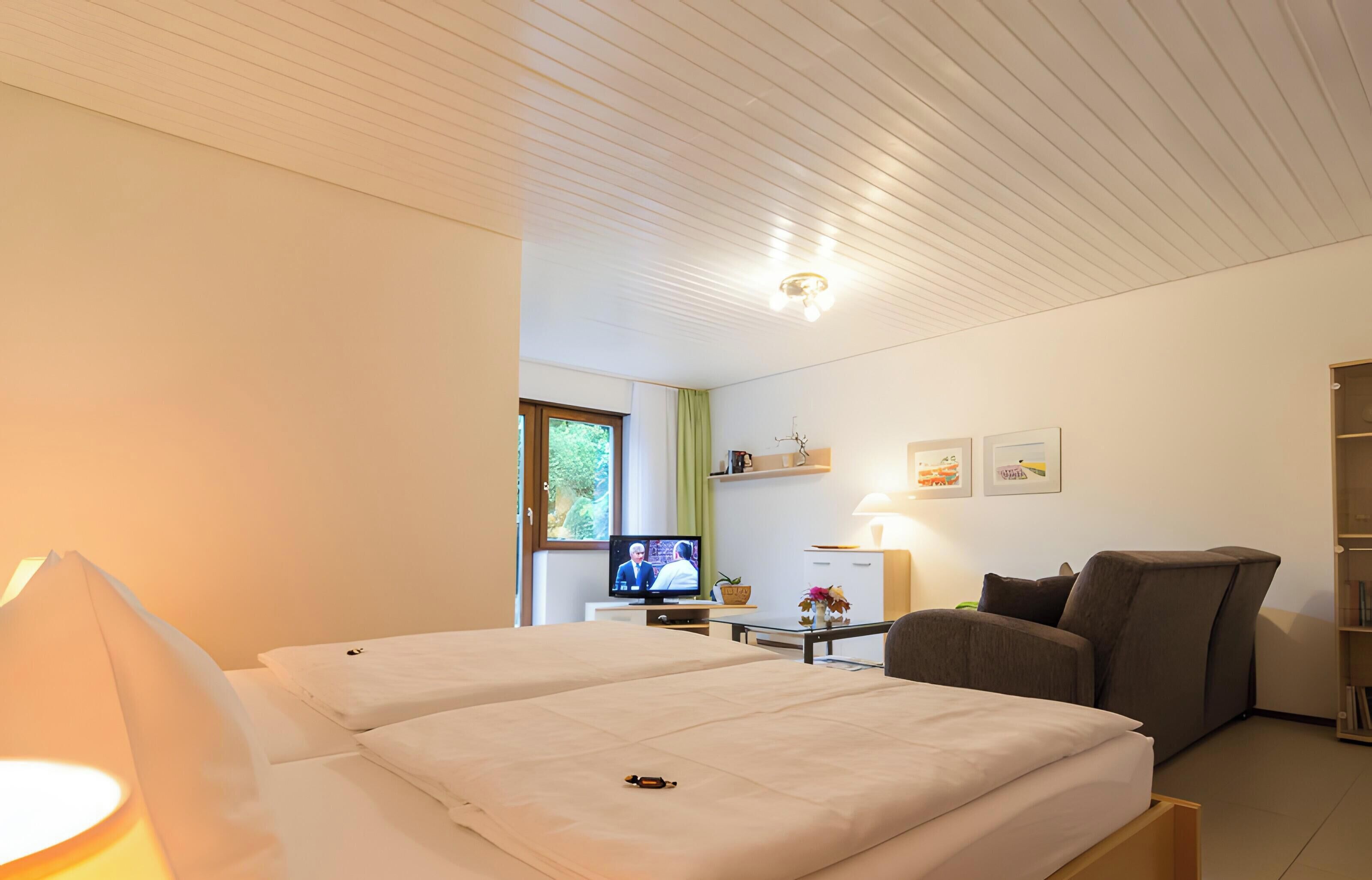 Ein Hotelzimmer mit Bett, Fernseher, Sessel, Schreibtisch und Bücherregal.