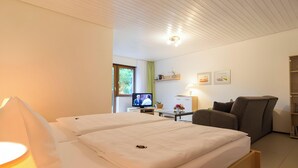 A hotel room with a bed, a TV, a chair, a desk, and a bookshelf. - Apartment 'Bergfrieden' with Private Terrace, Shared Garden and Wi-Fi (Bad Herrenalb)