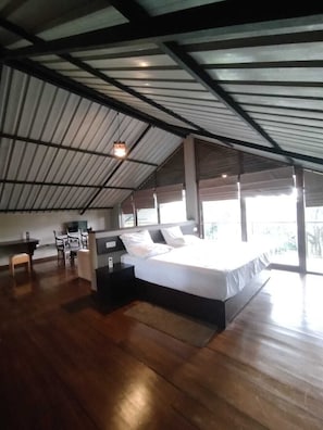 A spacious room with a large bed, a desk, and a chair, featuring a high ceiling and large windows. - AHAS GAWWA Eco Lodge (Padukka)