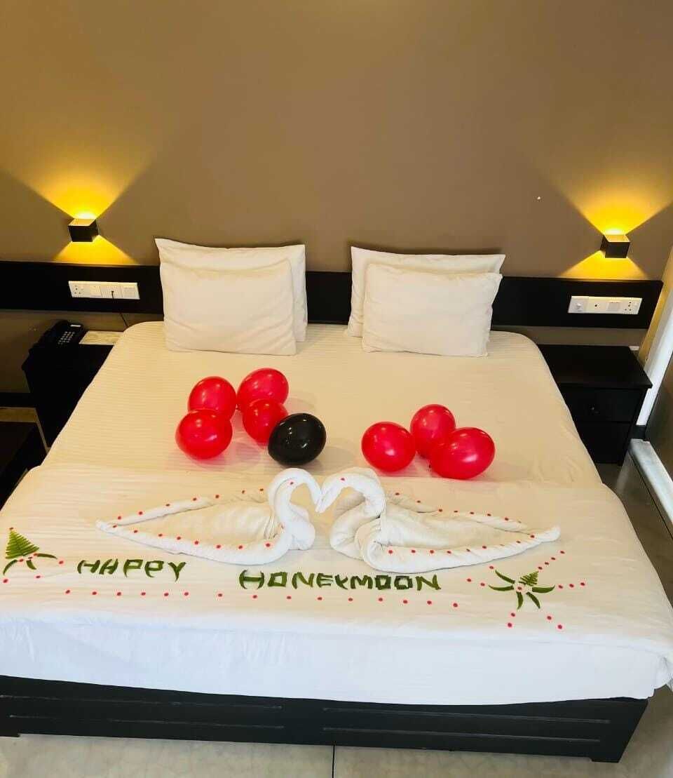 A hotel room with a bed, pillows, a bedside table, a lamp, and a decorative arrangement on the bed.