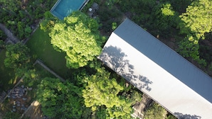 Vista aérea de una propiedad con piscina, abundante vegetación y un edificio grande con techo inclinado.