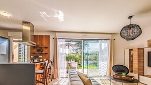 Ein modernes Wohnzimmer mit einer Couch, einem Essbereich mit Stühlen, einer Küche mit Herd und einer großen Schiebetür, die zu einem Garten führt.