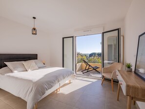 Une chambre à coucher comprenant un lit, un bureau, une chaise et un balcon avec vue sur la campagne.