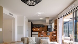 Ein modernes Wohnzimmer mit einer Eckcouch, einem Essbereich mit Holzsesseln und einer Küche mit schwarzer Arbeitsplatte.