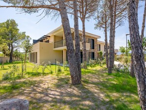 Une maison moderne à deux étages, dotée d’un balcon, entourée d’arbres et d’un jardin clos.