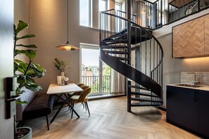 Una cucina moderna con una scala a chiocciola nera, un'area pranzo con tavolo e sedie, e un'ampia finestra vista edifici.