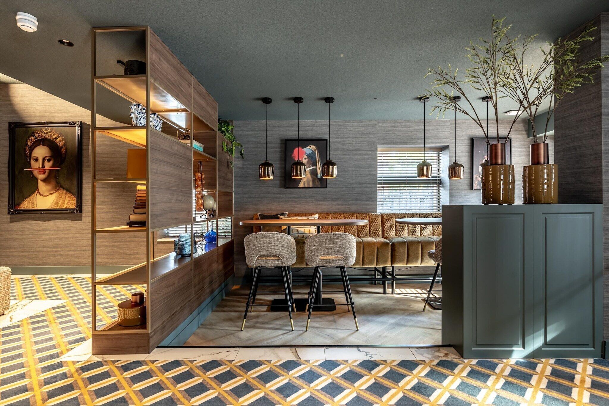Un intérieur moderne avec une bibliothèque en bois, deux tabourets de bar, une table à manger et des lampes suspendues.