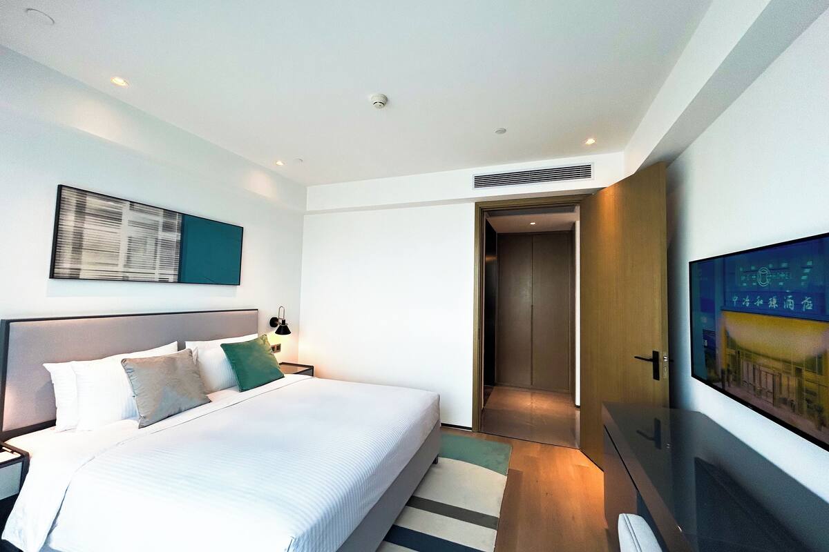 Habitación de hotel moderna con una cama grande, un televisor de pantalla plana y una puerta que da a un pasillo.