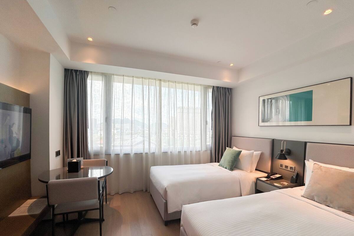 Habitación de hotel con dos camas, un escritorio, una silla, un televisor y un cuadro en la pared.