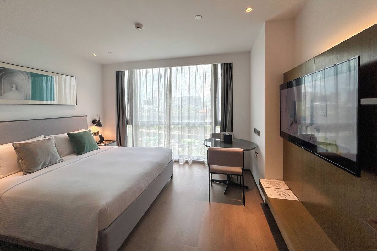 Una habitación de hotel con una cama grande, un escritorio, una silla, un televisor y una ventana con cortinas.