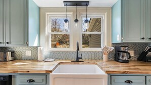 A kitchen with a large sink, wooden countertops, light blue cabinets, and a window with a view of trees.