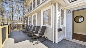 A covered outdoor seating area with multiple chairs, a wooden deck, and a building with large windows and a garage door.
