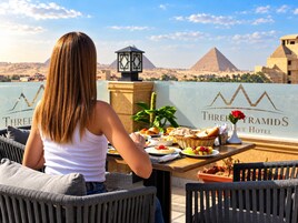 Una persona cena a un tavolo con vista sulle piramidi, una lampada e un cartello dell'Hotel Three Pyramids.