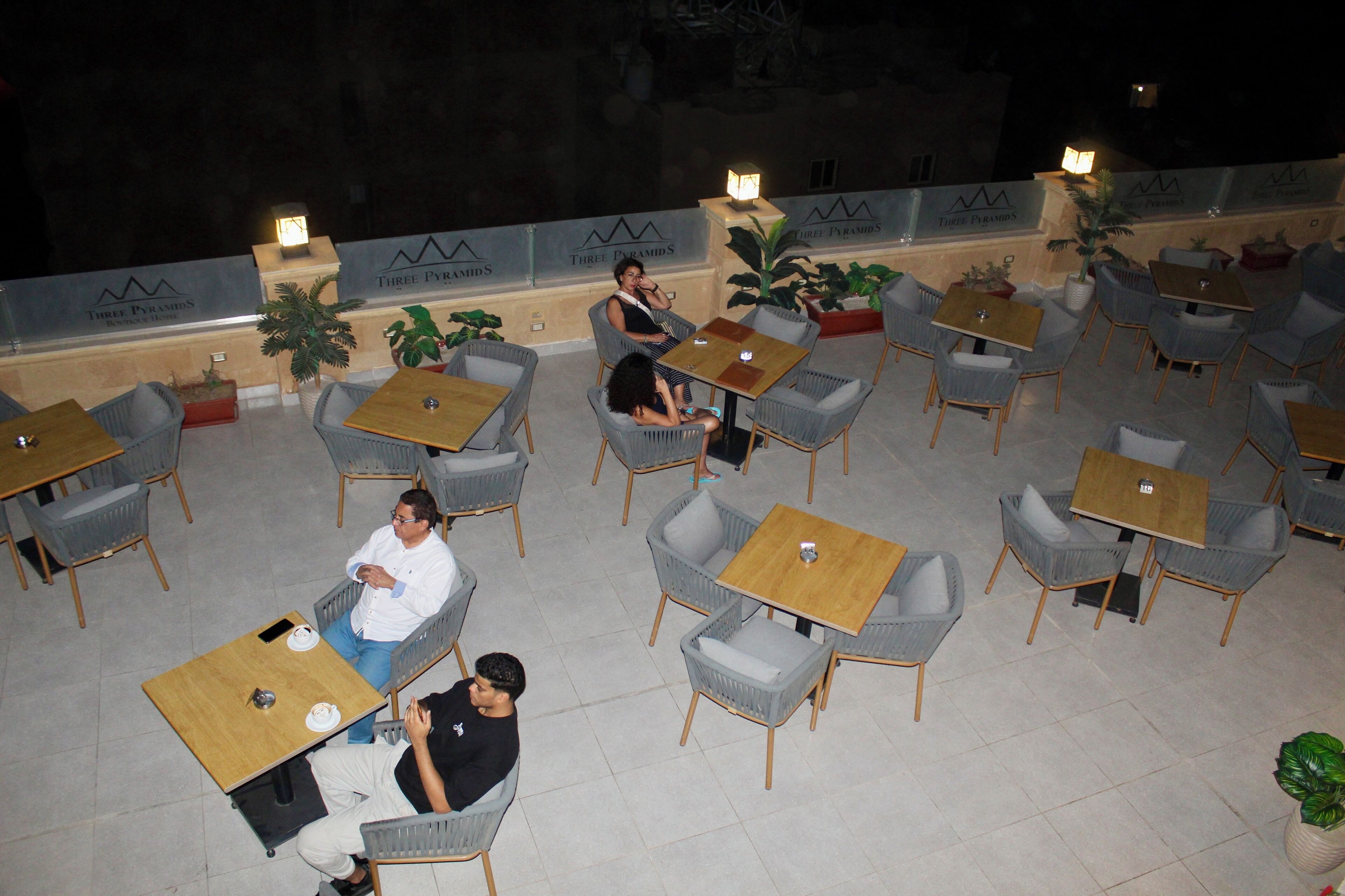 An outdoor seating area with wicker chairs and tables, potted plants, and a tiled floor.