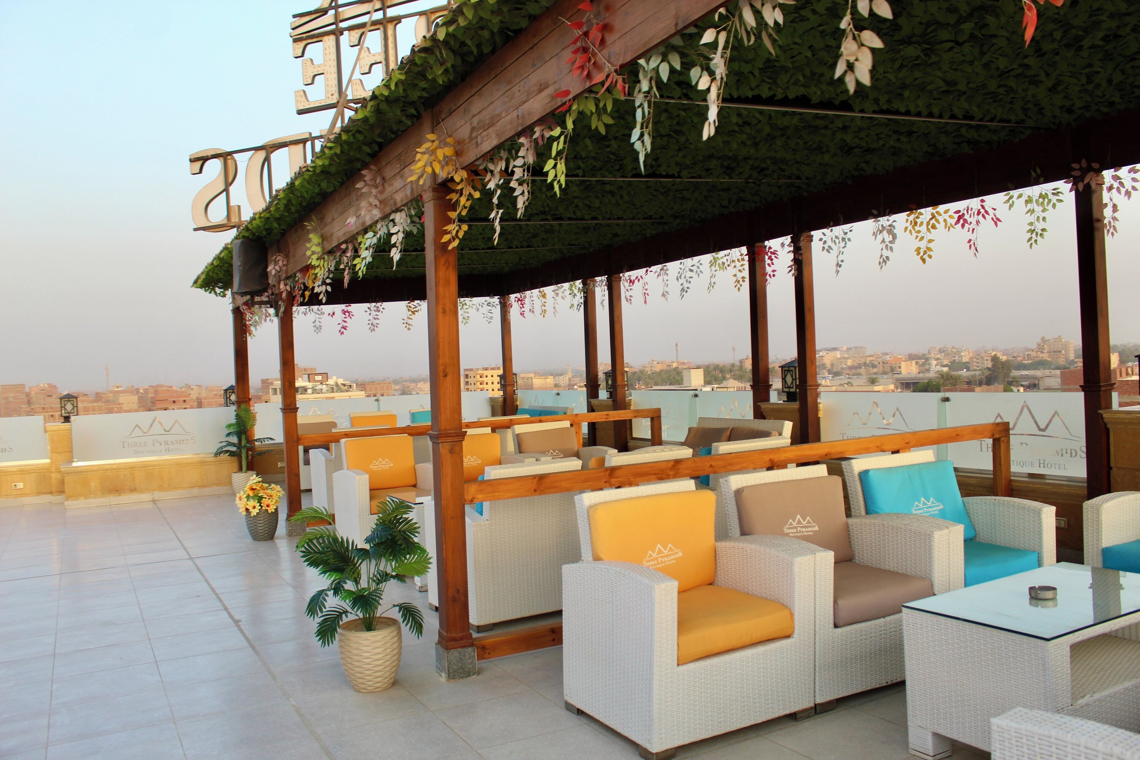A rooftop terrace with wicker furniture, a wooden pergola, and a view of the cityscape.