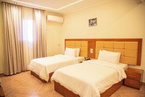 A hotel room with two beds, a wooden headboard, a nightstand, and a window with curtains. - Three Pyramids Boutique Hotel (Giza)