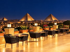 A rooftop terrace with tables and chairs, overlooking the pyramids at night.
